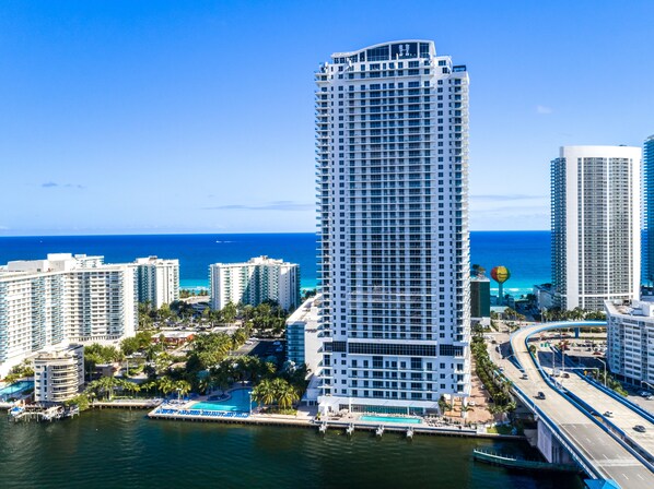 A high-rise hotel with a pool, located near a coastal area with other buildings and a bridge. - NEW 2019 Condo, 1Bedroom+2 Bathrooms, Amazing Views@HydeResort (Hollywood)