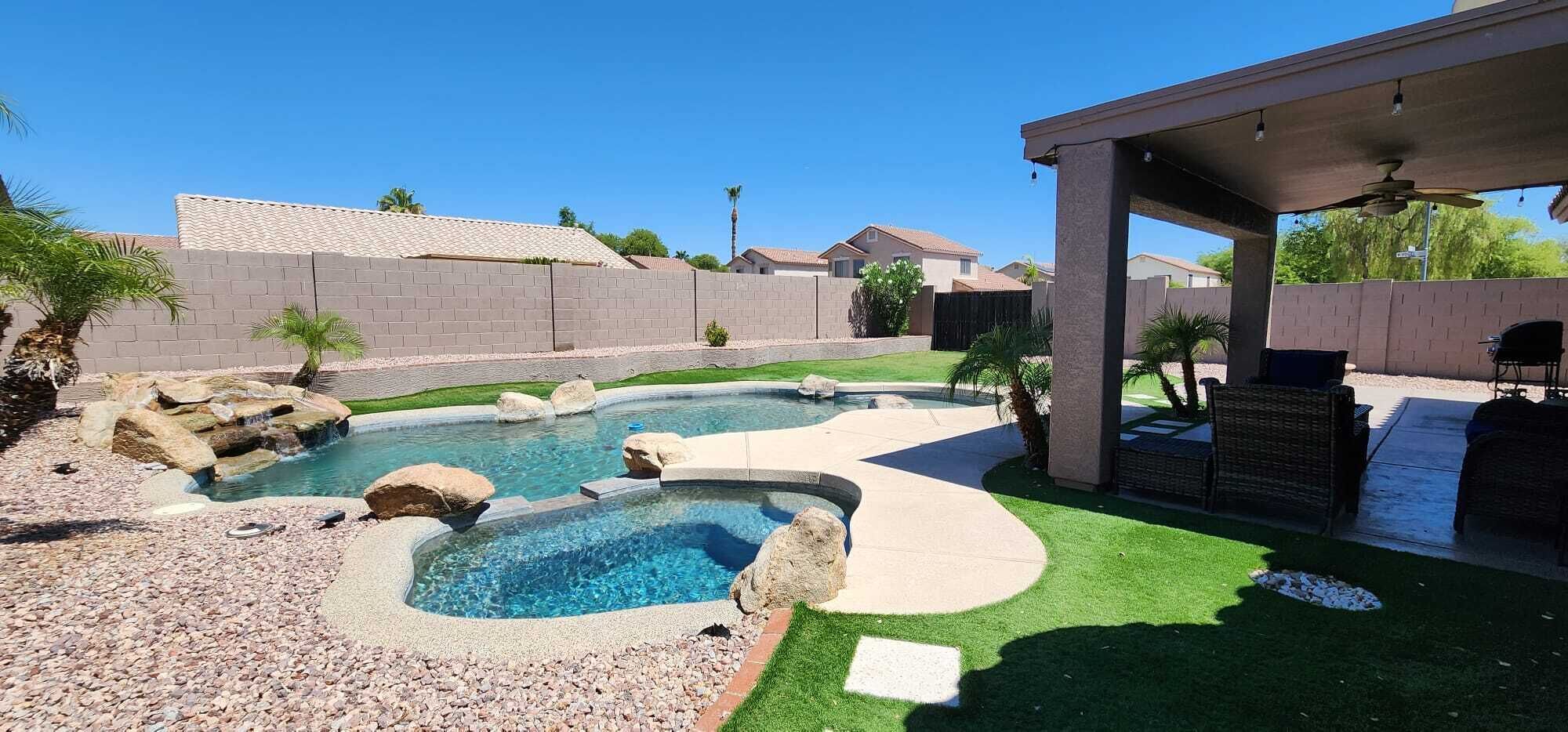 A backyard with a swimming pool, a covered patio, and a well-maintained lawn.