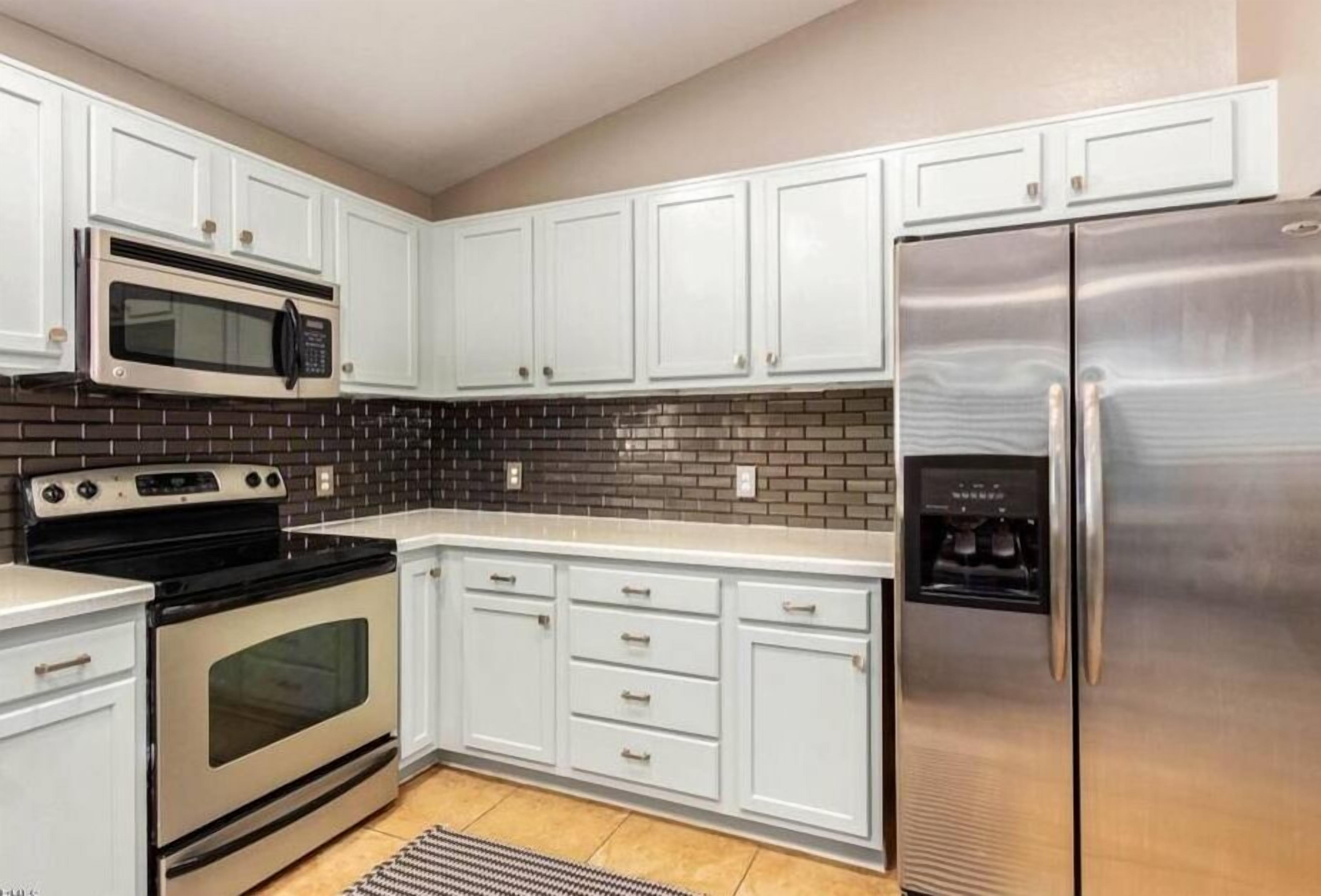 A kitchen with white cabinets, a stainless steel refrigerator, a microwave, and a double oven.