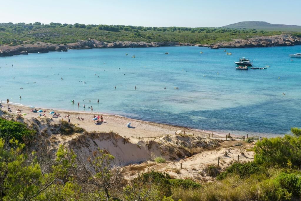 A coastal beach with clear blue waters, sandy shores, and boats.