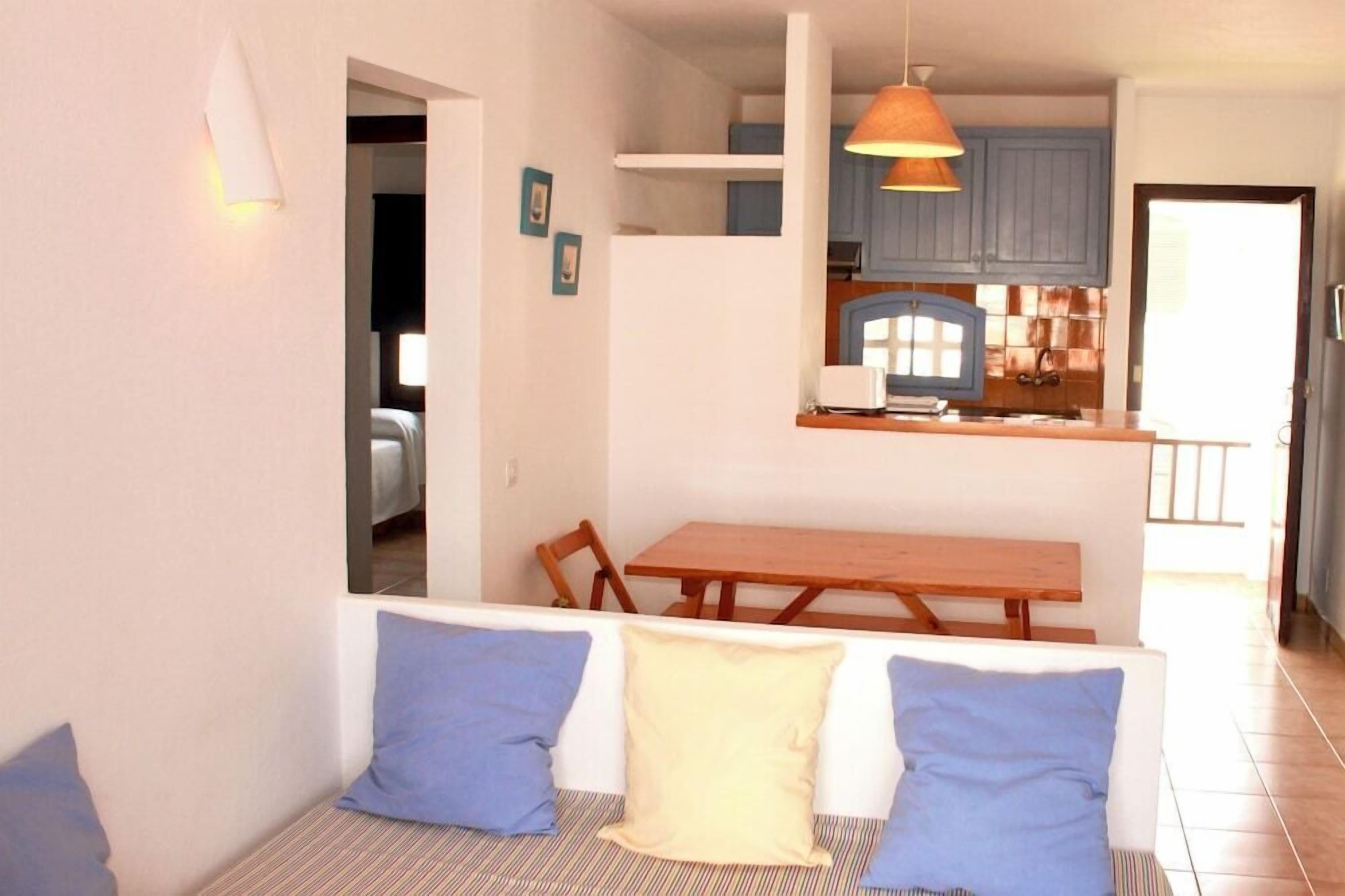 Un espacio habitable compacto con comedor, kitchenette y sofá con cojines.