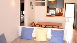 A compact living space with a dining area, kitchenette, and a sofa with cushions. - Apartamentos Posidonia (Mercadal)