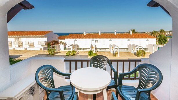 Un balcon avec une table et des chaises, donnant sur une zone côtière avec des bâtiments et un ciel dégagé.