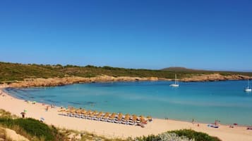 Una playa con aguas azules cristalinas, una orilla arenosa y una hilera de sombrillas.