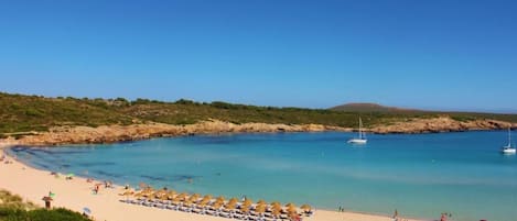 Una playa con aguas azules cristalinas, una orilla arenosa y una hilera de sombrillas.
