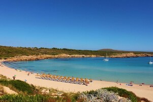 Una playa con aguas azules cristalinas, una orilla arenosa y una hilera de sombrillas.