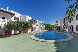 Una piscina rodeada de edificios blancos con balcones, cielo azul despejado y una palmera.
