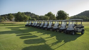 A row of golf carts lined up on a well-maintained golf course with a clear sky and trees in the background. - Apartamentos Posidonia (Mercadal)