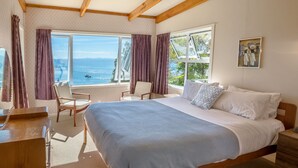 Une chambre avec un grand lit, deux fauteuils, un bureau et une vue sur la mer.