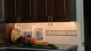 Una cocina con gabinetes marrón oscuro, encimera de vidrio y salpicadero de azulejos.