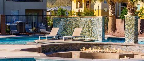 A swimming pool with lounge chairs, a decorative wall, and a mountain in the background.