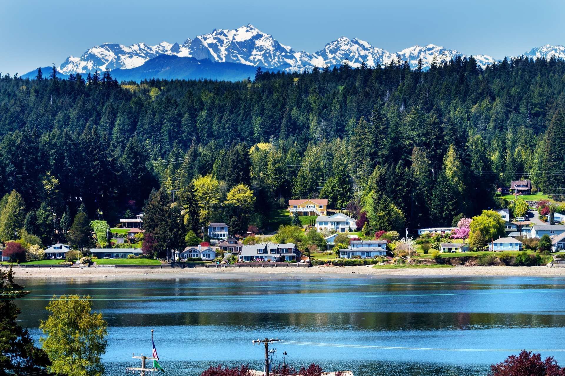 Un quartier résidentiel au bord d’un lac, avec des maisons, un quai et une chaîne de montagnes en arrière-plan.