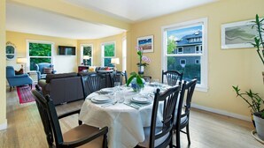 A dining area with a table set for four, surrounded by chairs, a sofa, and a television.