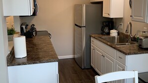 A compact kitchen with white cabinets, a stainless steel refrigerator, a granite countertop, and a round dining table with a white placemat.