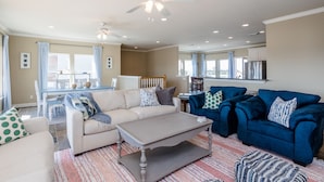 A spacious living room with a beige sofa, a blue sofa, and a coffee table. There is a dining area with a table and chairs in the background.