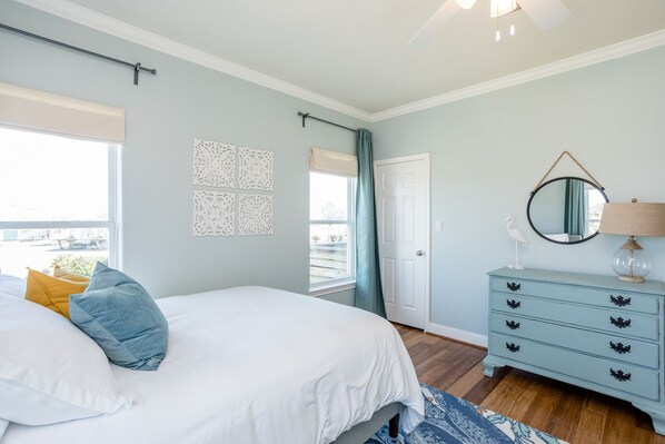A bedroom with a bed, a dresser, a mirror, and a window with curtains.