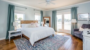 A bedroom with a large bed, a ceiling fan, a nightstand, a dresser, and a view of the outdoors.