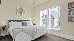 A bedroom with a large window, a bed with white bedding, a nightstand with a lamp, and a wall-mounted artwork. - Work Here!! King Bed, 400+ Mbps WiFi, BYU (Provo)