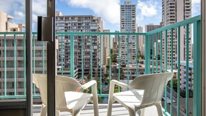 Een balkon met twee witte stoelen, een metalen hekwerk en uitzicht op hoge gebouwen.
