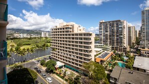 Een hoog hotel met meerdere verdiepingen, een zwembad en uitzicht op een rivier en bergen op de achtergrond.