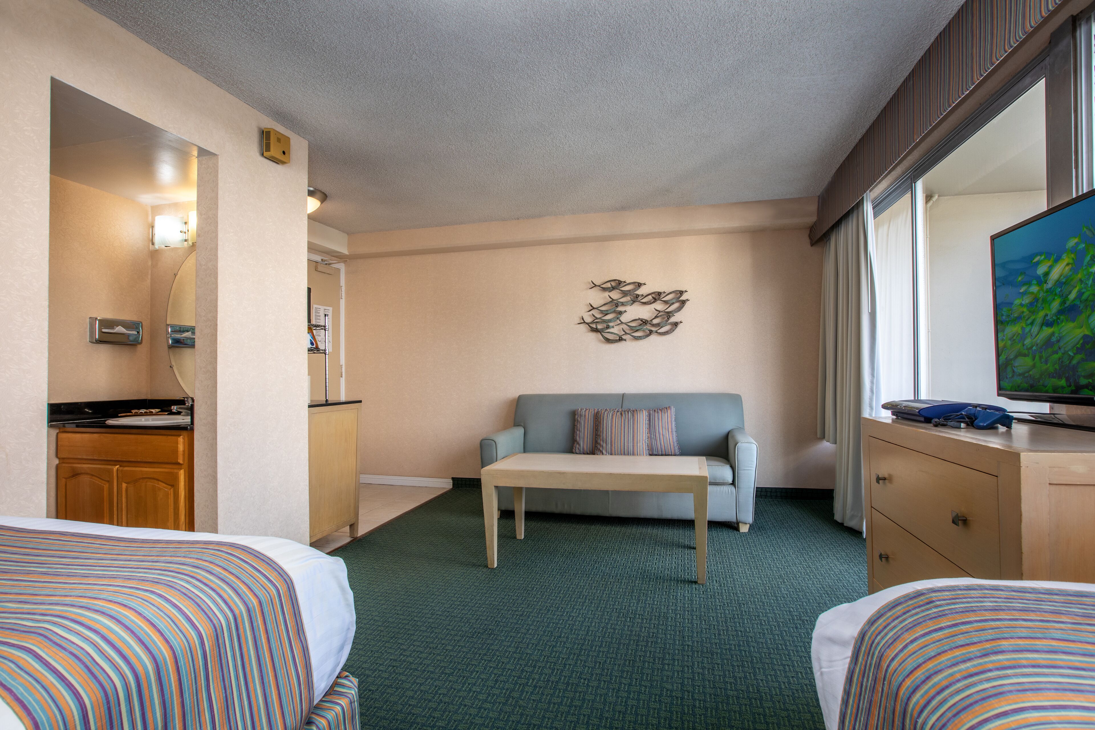 A hotel room with two beds, a sofa, a small table, a TV, and a kitchenette.