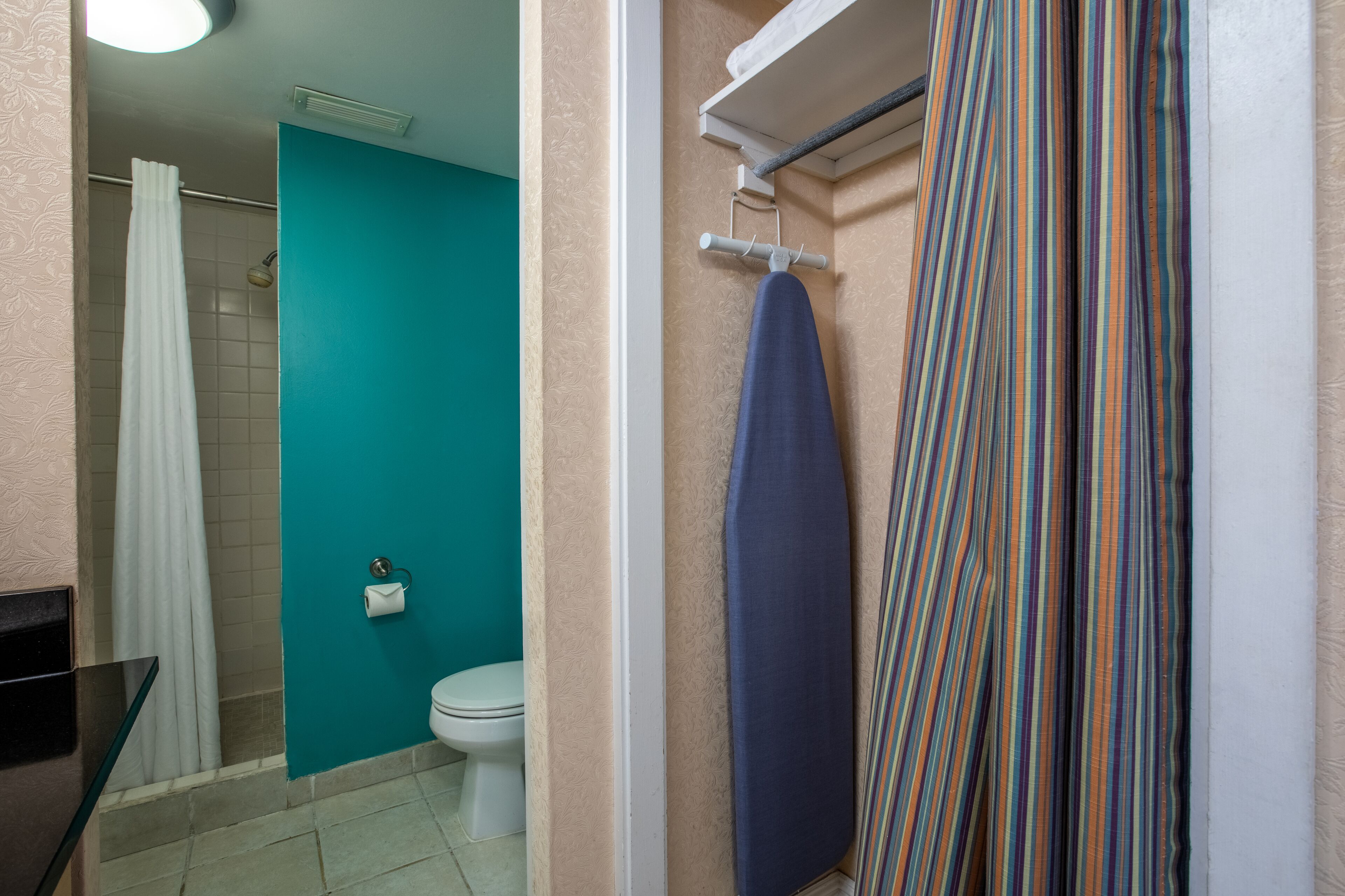 A bathroom with a toilet, a shower with a white curtain, and a towel rack with a striped towel.