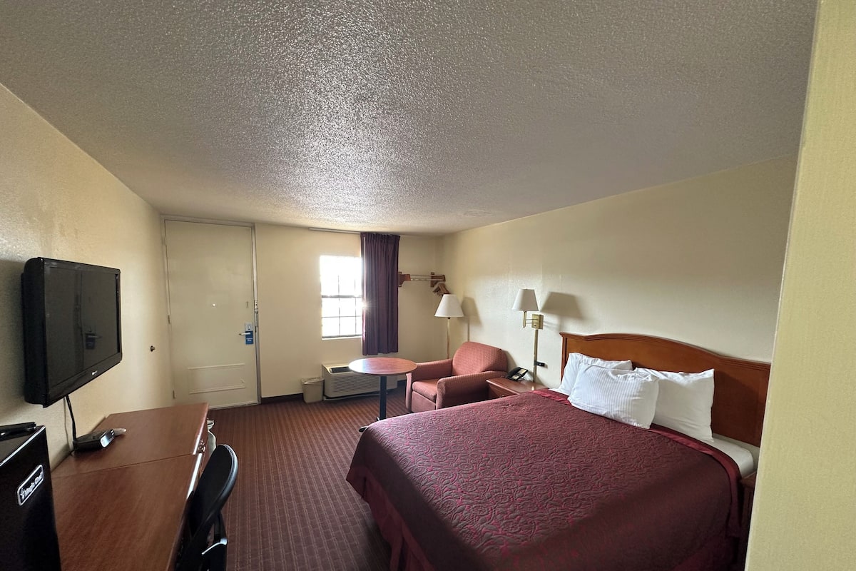 A hotel room with a bed, a desk, a chair, a television, and a window with curtains.