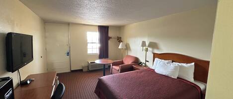 A hotel room with a bed, a desk, a chair, a television, and a window with curtains.