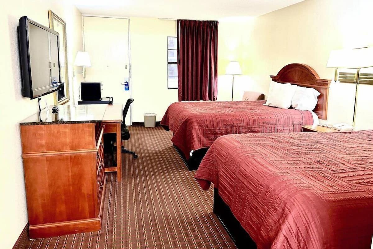 A hotel room with two beds, a desk, a TV, and a chair.