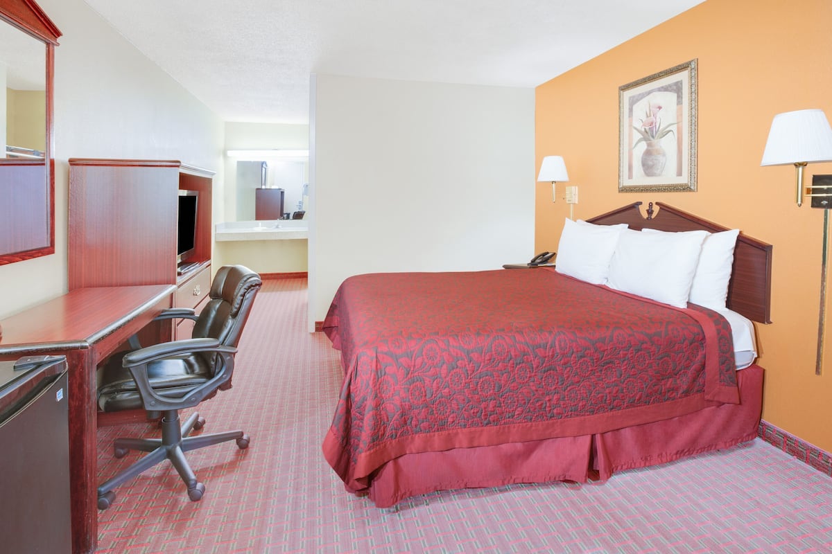 A hotel room with a bed, desk, chair, and a television.