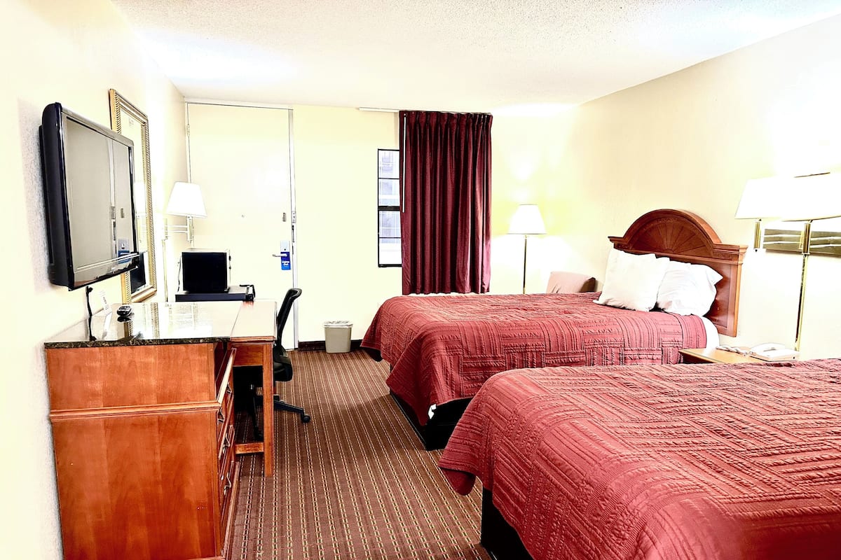 A hotel room with two beds, a desk, a chair, a TV, and a mirror.