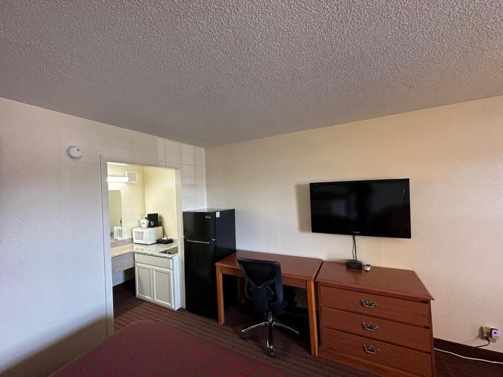 Habitación de hotel con kitchenette, un escritorio, una silla, televisor de pantalla plana y cómoda de madera.