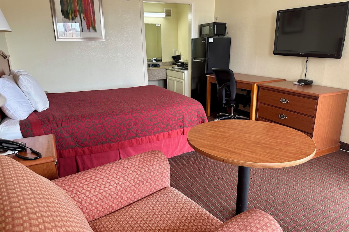 A hotel room with a bed, a desk, a chair, a TV, and a small table.