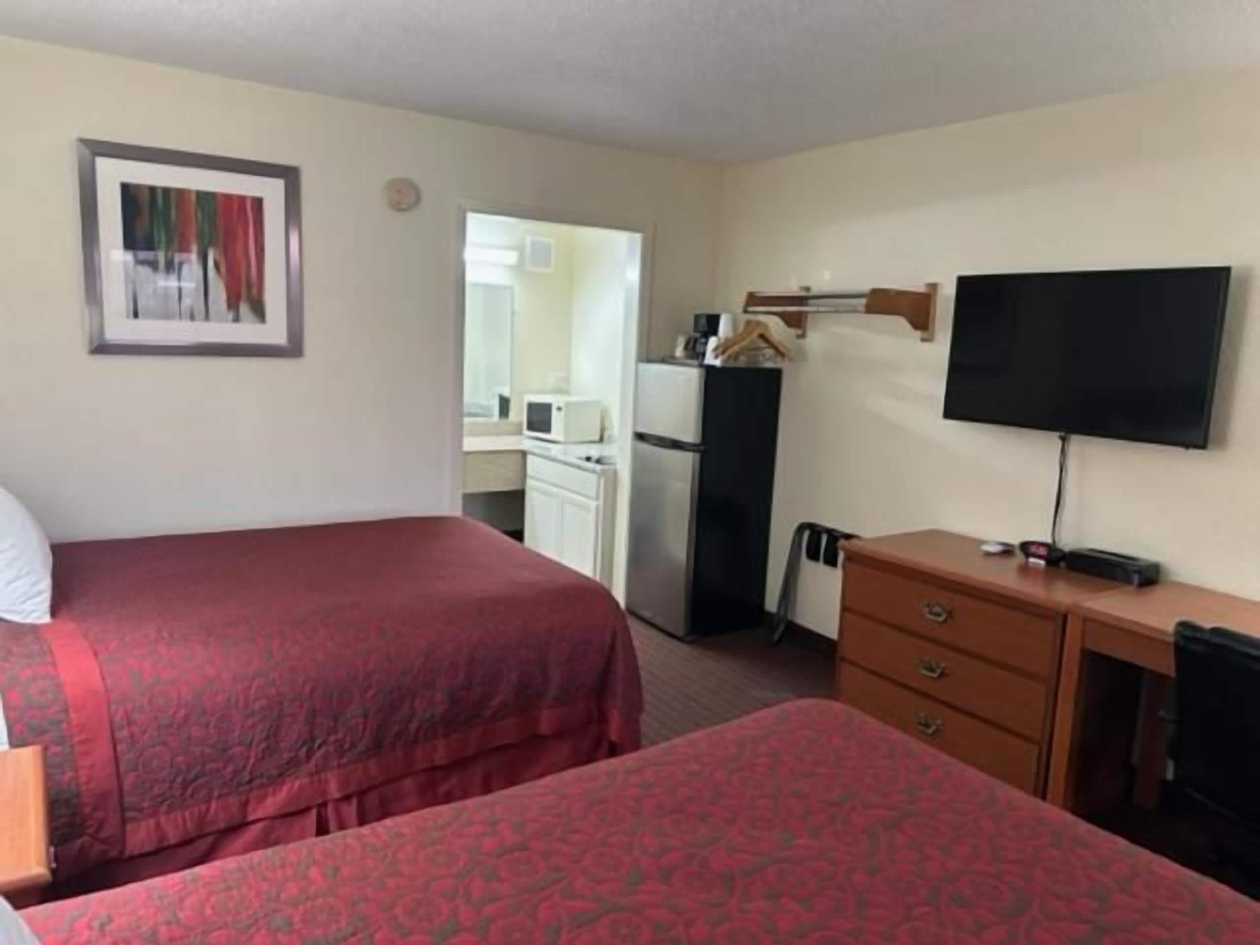 A hotel room with two beds, a television, a desk, and a kitchenette.
