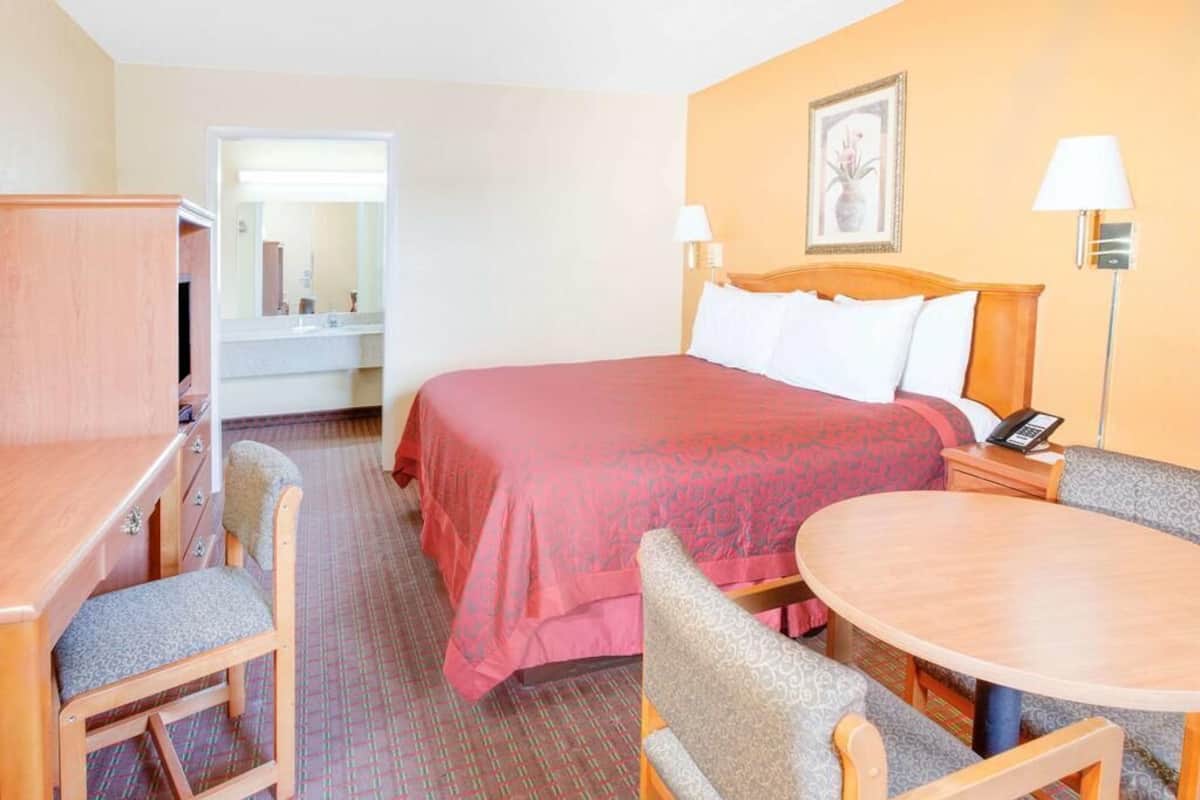 A hotel room with a bed, a desk with a chair, a small table, and a mirror.