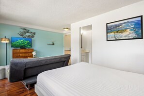A bedroom with a bed, a sofa, a TV, a wooden dresser, and a painting on the wall. - Aqua Aloha Surf Waikiki 1107 | Downtown City Views – Pool & BBQ (Honolulu)