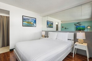 A hotel room with a bed, a nightstand, a mirror, and two framed pictures on the wall.
