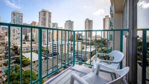 A balcony with a view of a cityscape, including high-rise buildings and a clear sky. - Aqua Aloha Surf Waikiki 1112 | Sparkling City Views – Pool & BBQ (Honolulu)