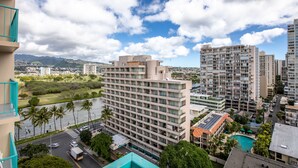 A high-rise hotel with multiple floors, a swimming pool, and a view of a river and mountains in the background.