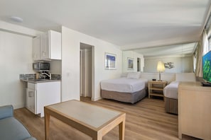 Une chambre d’hôtel équipée d’une kitchenette, d’un lit, d’une petite table, d’une table de chevet et d’un téléviseur.