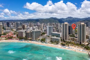 A coastal cityscape with high-rise buildings, a beach, and mountains in the background.