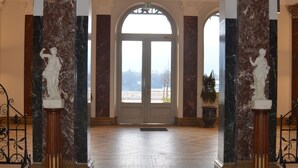 Un'imponente hall con colonne in marmo, un'ampia porta ad arco e vista su un edificio sullo sfondo.