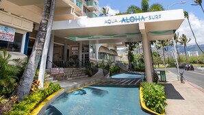 A hotel with a pool area, palm trees, and a sign reading "AQUA ALOHA SURF".