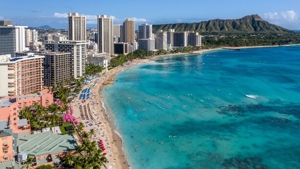 A coastal cityscape with high-rise buildings, a beach, and a mountain in the background.