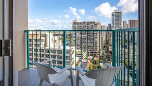 A balcony with two white chairs, a green railing, and a view of high-rise buildings.