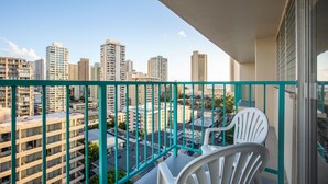A balcony with a view of high-rise buildings, a table, and two white chairs.