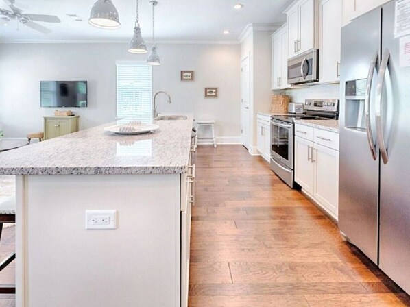 A modern kitchen with a granite countertop, stainless steel appliances, and a wooden floor.