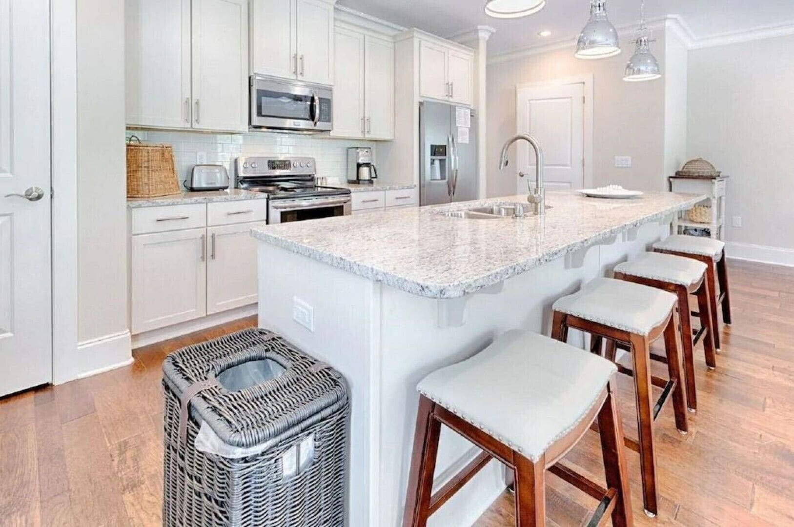 A modern kitchen with white cabinets, stainless steel appliances, a granite countertop, and bar stools.
