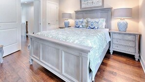 A bedroom with a large bed, two bedside tables, a dresser, and a door leading to another room. - Shore Do Love You: 5BR, Sleeps 12, Heated Private Pool & Optional Hot Tub! (Santa Rosa Beach)