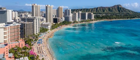Un paisaje costero con edificios altos, una playa y una montaña al fondo.